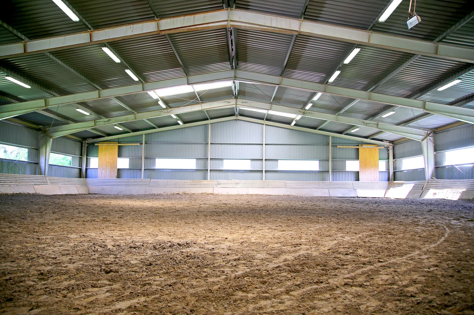 Inside a clear span indoor riding arena with a sand surface and roof lights