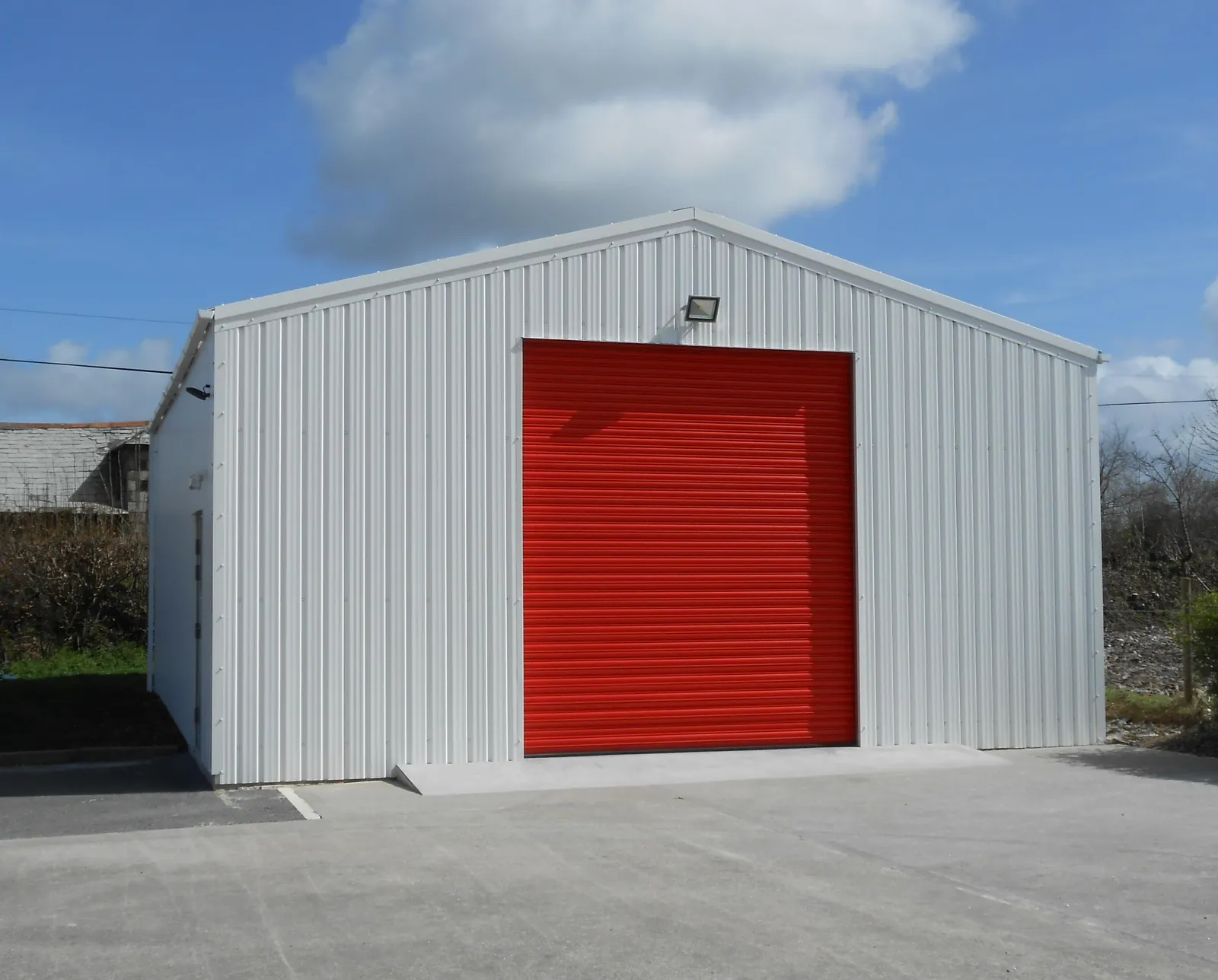 White clad industrial unit with a red roller shutter door